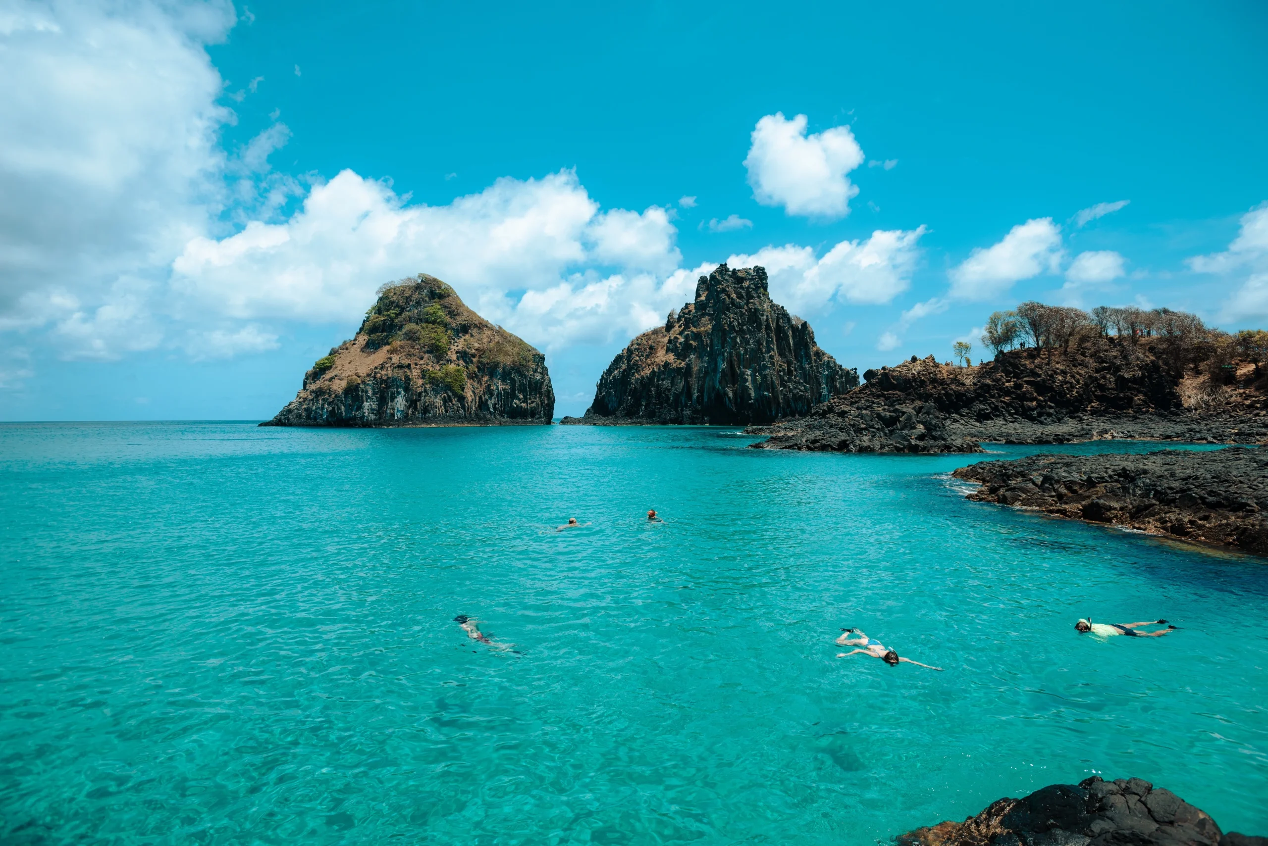 Vista aérea de uma praia paradisíaca em Fernando de Noronha, com morros e mar azul-turquesa.
